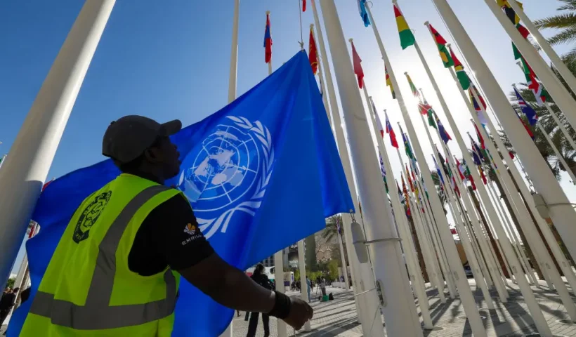 A worker prepares to hoist a United Nations flag with other national flags of participating countries at the venue of the COP28 UN climate summit in Dubai on November 30, 2023. The UN climate conference opens in Dubai on November 30 with nations under pressure to increase the urgency of action on global warming and wean off fossil fuels, amid intense scrutiny of oil-rich hosts UAE. (Photo by Giuseppe CACACE / AFP) (Photo by GIUSEPPE CACACE/AFP via Getty Images)