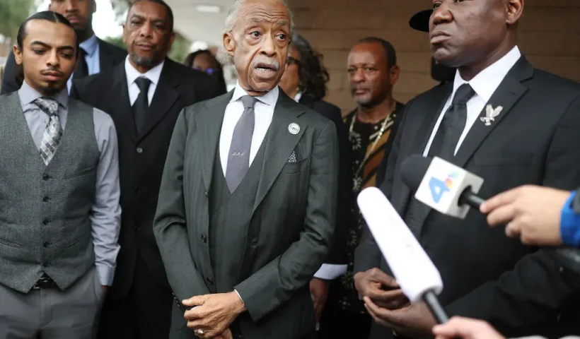 PASADENA, CALIFORNIA - FEBRUARY 06: Reverend Al Sharpton (C) and civil rights attorney Ben Crump (R) speak to the media as Trevor Kelley (3rd L) and Trevor Kelley Jr. (L), son and grandson of Erliene Kelley who died in the Eaton Fire, look on before a memorial service for area wildfire victims at First AME Church on February 6, 2025 in Pasadena, California. At least 29 people were killed and over 12,000 structures, many of them homes and businesses, were destroyed in the Eaton and Palisades Fires. (Photo by Mario Tama/Getty Images)
