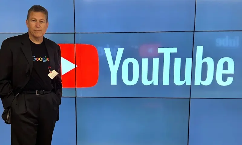 Charles Herring, president of OAN, proudly wearing a Google shirt while standing in front of a screen with the YouTube logo.