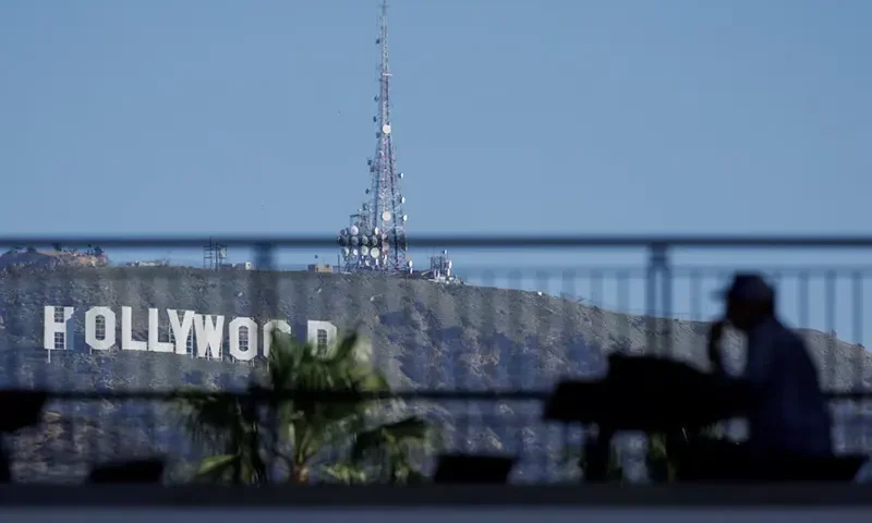 The iconic Hollywood sign is shown behind a person sitting in the shade along Hollywood Blvd as the city prepares to host the 97th Academy Awards in Los Angeles, California, U.S., February 25, 2025. REUTERS/MIKE BLAKE