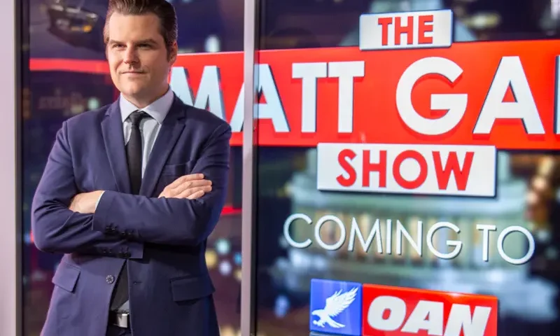 Matt Gaetz stands in front of a big screen promoting his new show on OAN, The Matt Gaetz Show.