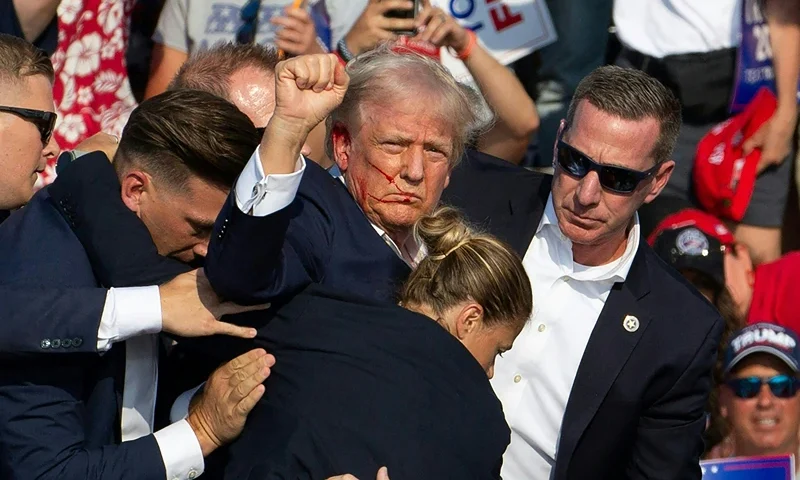 TOPSHOT - Republican candidate Donald Trump is seen with blood on his face surrounded by secret service agents as he is taken off the stage at a campaign event at Butler Farm Show Inc. in Butler, Pennsylvania, July 13, 2024. Donald Trump was hit in the ear in an apparent assassination attempt by a gunman at a campaign rally on Saturday, in a chaotic and shocking incident that will fuel fears of instability ahead of the 2024 US presidential election. The 78-year-old former president was rushed off stage with blood smeared across his face after the shooting in Butler, Pennsylvania, while the gunman and a bystander were killed and two spectators critically injured. (Photo by Rebecca DROKE / AFP) (Photo by REBECCA DROKE/AFP via Getty Images)