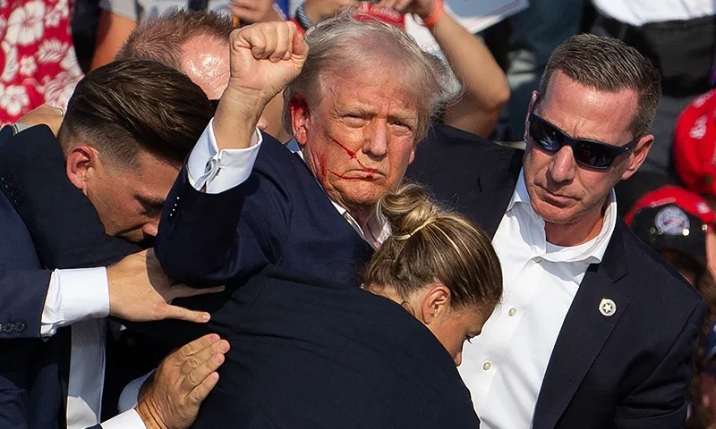 US Republican candidate Donald Trump is seen with blood on his face surrounded by secret service agents as he is taken off the stage at a campaign event at Butler Farm Show Inc. in Butler, Pennsylvania, on July 13, 2024. Trump was hit in the ear in an apparent assassination attempt by a gunman at a campaign rally on Saturday, in a chaotic and shocking incident that will fuel fears of instability ahead of the 2024 US presidential election. The 78-year-old former president was rushed off stage with blood smeared across his face after the shooting in Butler, Pennsylvania, while the gunman and a bystander were killed and two spectators critically injured. (Photo by Rebecca DROKE / AFP) / QUALITY REPEAT (Photo by REBECCA DROKE/AFP via Getty Images)