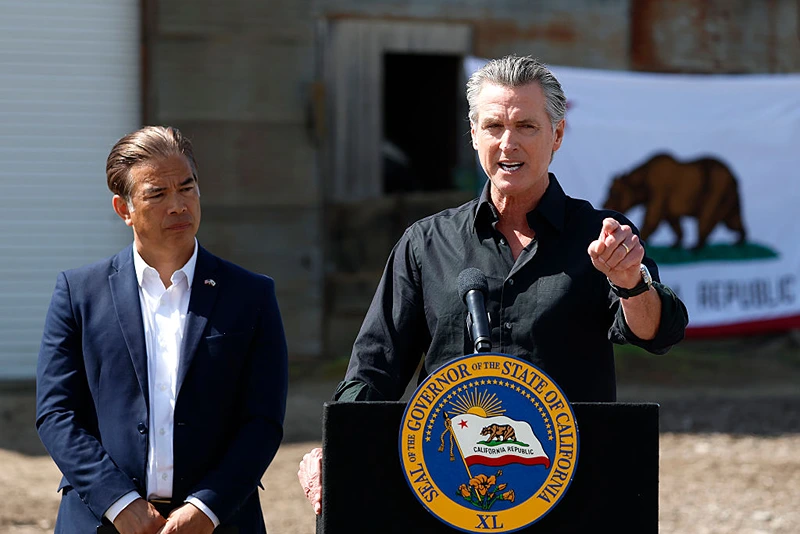 CERES, CALIFORNIA - APRIL 16: California Governor Gavin Newsom (R) speaks as  California Attorney general Rob Bonta looks on during a news conference at Gemperle Orchard on April 16, 2025 in Ceres, California. Governor Gavin Newsom and California Attorney General Rob Bonta have filed a lawsuit in federal court challenging the Trump administration's use of emergency powers to enact sweeping tariffs that hurt states, consumers, and businesses. The tariffs have disrupted supply chains, increased costs for the state and Californians, and inflicted billions in damages on California’s economy, the fifth largest in the world. (Photo by Justin Sullivan/Getty Images)