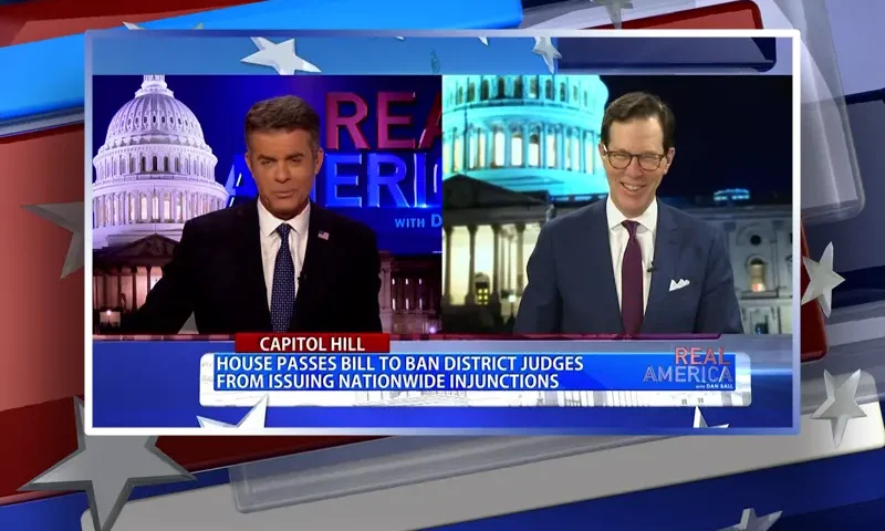 Video still from Real America on One America News Network showing a split screen of the host on the left side, and on the right side is the guest, John Hines.