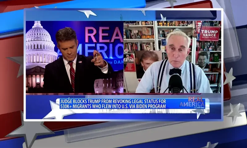 Video still from Real America on One America News Network showing a split screen of the host on the left side, and on the right side is the guest, Roger Stone.