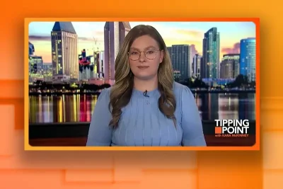 Video still of the host of Tipping Point at the desk of their talk show on One America News Network.