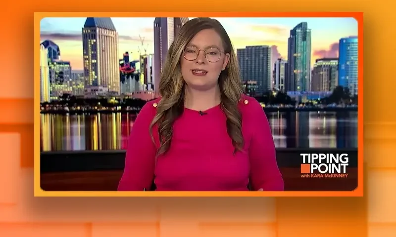 Video still of the host of Tipping Point at the desk of their talk show on One America News Network.